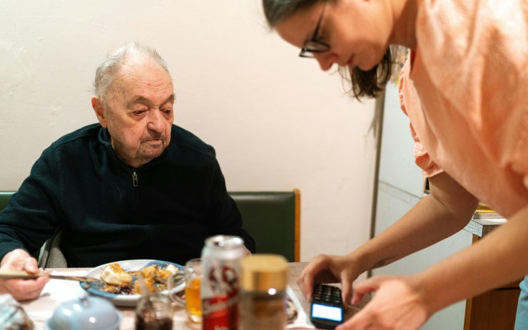 Anziano a tavola e nipote che lo serve e gli controlla il cellulare