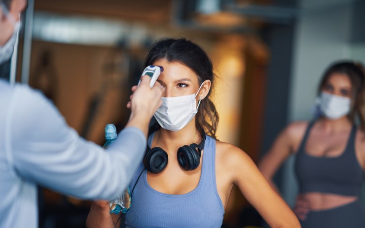 Uomo che misura la temperatura ad una ragazza che entra in palestra: le vecchie prassi anti Covid