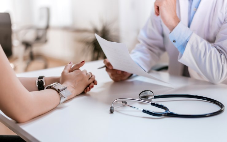 Medico che legge un foglio davanti alla paziente recata lì per la documentazione necessaria per il rinnovo della patente